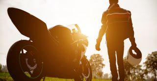 moottoripyörä ja vieressä seisova moottoripyöräilijä auringonlaskussa