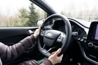 Nainen ajaa autoa kädet ratissa